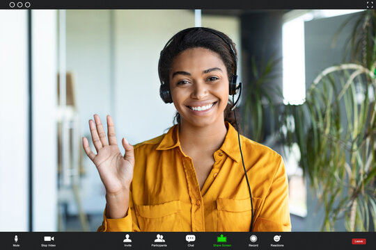 Positive african american businesswoman making video call from office, waving hand at camera and smiling, pov screenshot