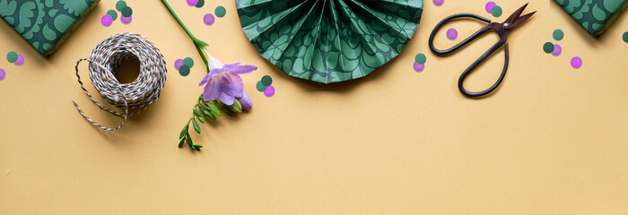 Spring flowers and gift boxes. Golden yellow paper background with green presents, scissors, cord....