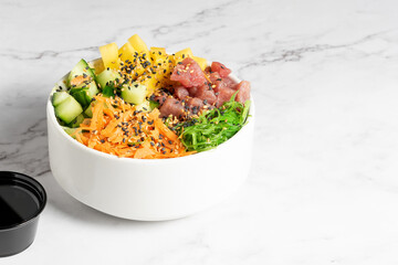 Tuna, carrot, cucumber and vegetable poke served in a white bowl on a marble table. High quality photo