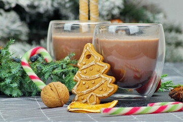 Two cups of hot chocolate will warm loving hearts in the cold winter season. The composition is complemented by a pine branch, a gingerbread tree in the shape of a Christmas tree and a warm atmosphere