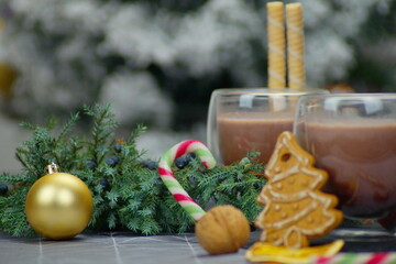 on a horizontal photo in transparent glasses - hot chocolate, cocoa, next to it are gingerbread cookies in the shape of a Christmas tree, caramel in the shape of a cane, nuts, orange pieces, tubules. 