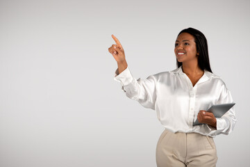 Happy young african american business woman with tablet points finger to empty space, controls virtual whiteboard