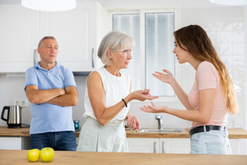 Elderly father tries to calm quarreled wife and daughter in the home kitchen