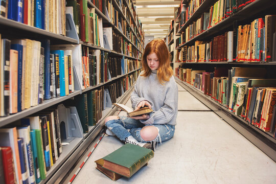 Teen girl sitting with book at the library.