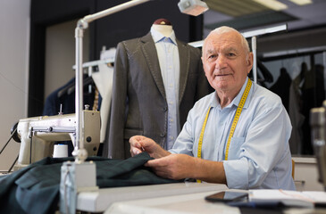 Elderly tailor sews lapel to a jacket in his workshop