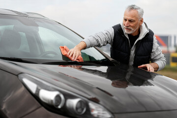 Senior man cleaning his car using micro fiber cloth. Car washing service concept