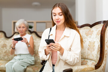 Elderly mother and adult daughter use the phone for various messengers in the home interior