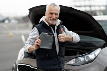 Senior man driver holds engine oil, shows thumb up, smiles at camera near his car with open hood 