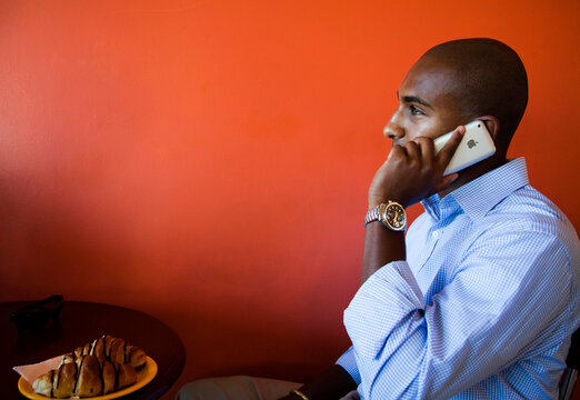 A young Ethiopian business man, talks on his cellular phone while city in a cafe with a bright red background