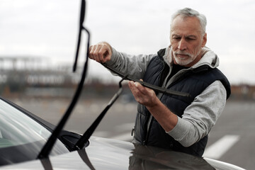 Portrait of senior man technician checking, changing, mounting new windscreen wiper on the car