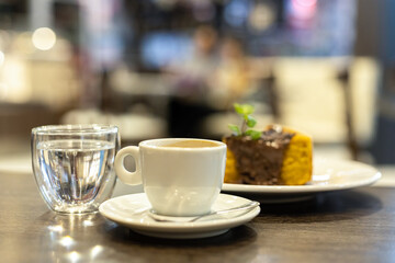 A mug of coffee, a glass of water, and a chocolate cake with mint leaves in a Brazilian café, with a blurred background