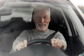 Handsome confident senior man driving new car on the road. Seat belt, safety driving concept