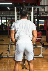 Fototapeta na wymiar Back side of a gym athlete wearing a white blank shirt doing weight lifting at a gym