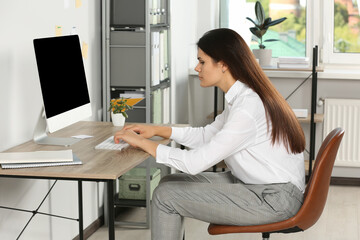 Young woman with bad posture sitting at workplace in office. Symptom of scoliosis - obrazy, fototapety, plakaty