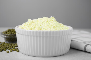 Mung bean flour in bowl and seeds on white table, closeup