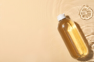 Wet bottle of micellar water on beige background, top view. Space for text