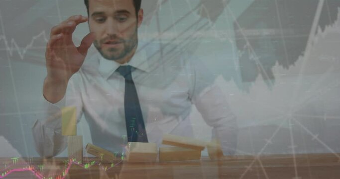 Animation of graphs and numbers over caucasian businessman playing with toy blocks falling on table - Powered by Adobe