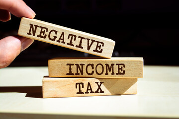Closeup on businessman holding a wooden blocks with text NEGATIVE INCOME TAX, business concept
