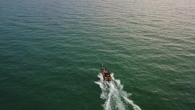 Aerial drone flyover shot capturing small traditional small fishing boat sailing on the sea at sunset.