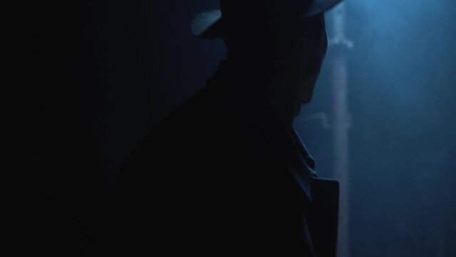 Old garage with blue light. Atmosphere dark place full of smoke. Strang and mystery man in black coat and black hat is walking 