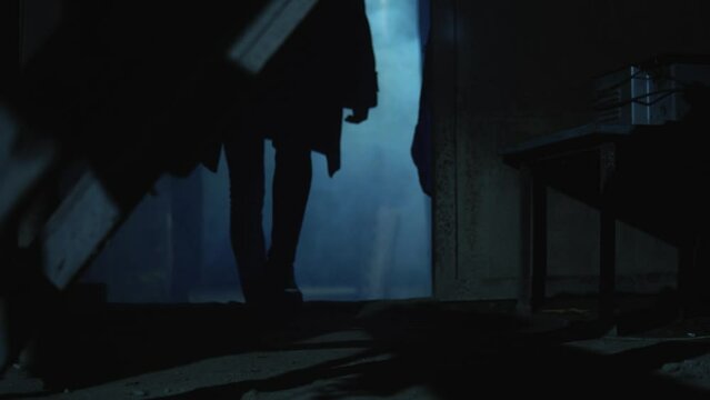 Old garage with blue light. Atmosphere dark place full of smoke. Strang and mystery man in black coat and black hat is walking 