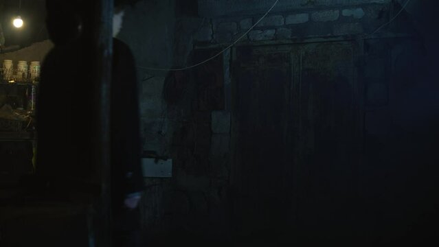 Old garage with blue light. Atmosphere dark place full of smoke. Strang and mystery man in black coat and black hat is walking 