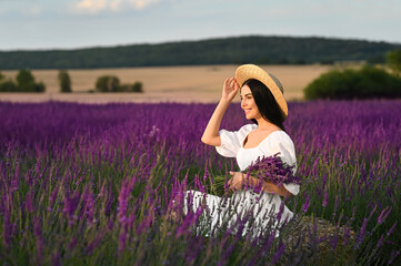 Fototapeta na wymiar Beautiful young woman with bouquet sitting in lavender field