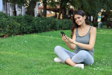 Fototapeta premium Young woman using smartphone on green grass in park