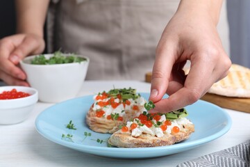 Obraz na płótnie Canvas Woman putting microgreens onto sandwich with caviar at table, closeup