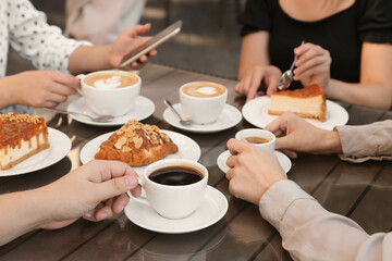 Friends drinking coffee at wooden table in outdoor cafe, closeup