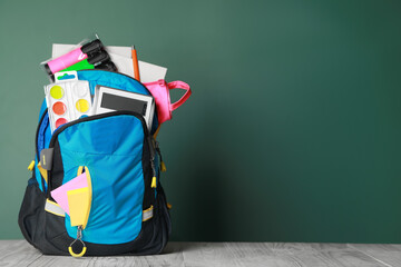 Backpack with different school stationery on wooden table near chalkboard, space for text
