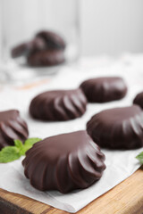 Delicious chocolate covered zephyrs and mint on wooden board, closeup. Space for text