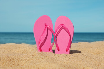 Fototapeta na wymiar Stylish pink slippers on sand near sea. Beach accessory