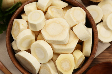Cut fresh ripe parsnip in bowl on wooden table, top view