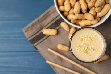 Glass of tasty banana smoothie with peanuts on light blue wooden table, flat lay. Space for text