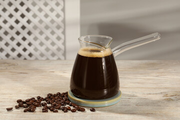 Glass turkish coffee pot with hot drink and beans on wooden table