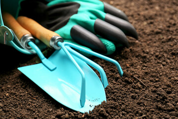 Overturned bucket with gardening tools and gloves on fresh soil, closeup