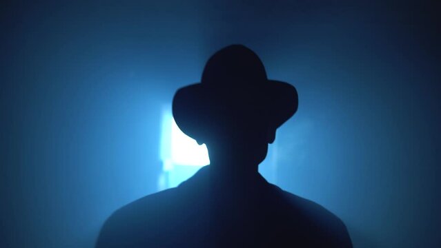 Old garage with blue light. Atmosphere dark place full of smoke. Strang and mystery man in black coat and black hat is talking