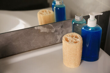 Obraz na płótnie Canvas Natural loofah sponge and shower gel bottles on washbasin in bathroom
