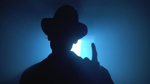 Old garage with blue light. Atmosphere dark place full of smoke. Strang and mystery man in black coat and black hat is talking