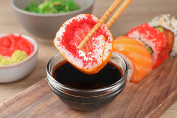 Holding delicious sushi roll with chopsticks at wooden table, closeup