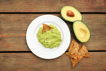 Delicious guacamole, avocado and nachos on wooden table, flat lay