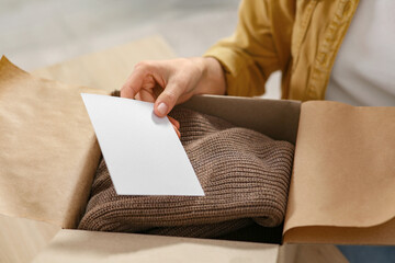 Woman holding greeting card near parcel with Christmas gift indoors, closeup