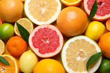 Different ripe citrus fruits with green leaves as background, top view