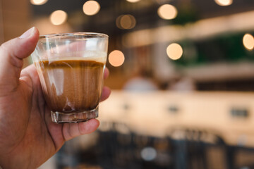 Man holding a glass of Mocha dirty coffee, pouring a mocha shot into a cup with frozen milk against on a bokeh background.