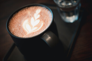 Glass of hot Mocha with latte art in black cup at cafe.