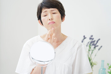 家で鏡をで顔を見て困っている中年女性