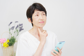 家でスマホを持って考える中年女性
