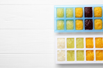 Different purees in ice cube trays ready for freezing on white wooden table, flat lay. Space for text