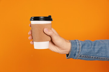 Woman holding takeaway cup with drink on orange background, closeup. Coffee to go